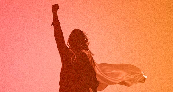 A hazy, orange-tinted image of the silhouette of a person wearing a cape with their fist raised victoriously in the air.