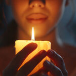 A woman cupping a lit candle between her hands.