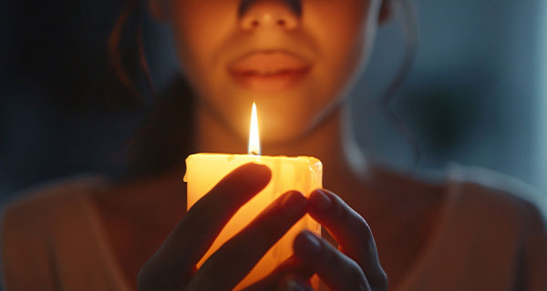 A woman cupping a lit candle between her hands.