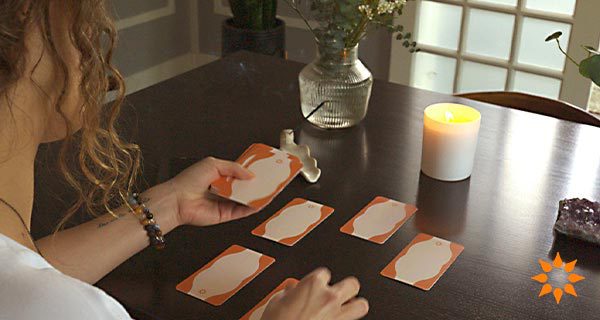 An image of a woman sitting by a table, laying out a psychic development Tarot spread.