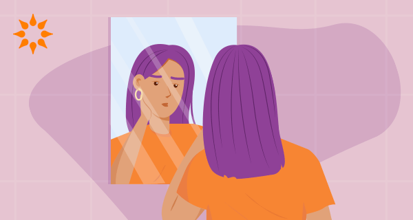 An image of a woman in a purple-haired woman in an orange shirt. She is looking in a mirror and trying to stand up for herself.