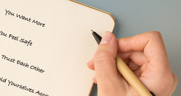 An image of someone writing in their journal. The desk behind them is blue, and the words are cut off, but they seem to be writing a list.