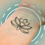 An image of a black outline lotus flower tattoo on the inside of someone's wrist.