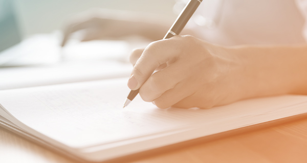 An orange-tinted image of someone's hand writing in a journal with a pen.