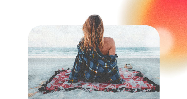 An image of a woman sitting on a blanket at a beach, looking out over the ocean.