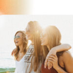 An image of three girls on the beach, facing off-camera at a diagonal angle as the sun sets behind them.
