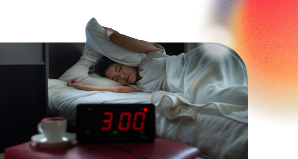 An image of a woman sleeping in bed with a pillow clapped over her head. The clock reads 3 A.M.