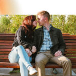 A young couple exchanges a kiss on a park bench.