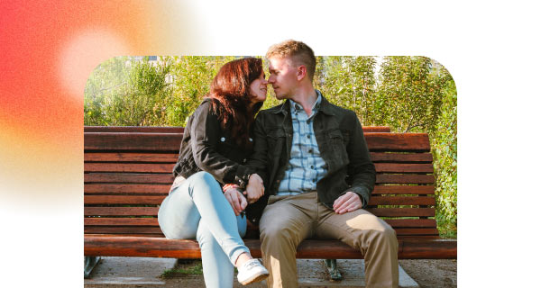 A young couple exchanges a kiss on a park bench.