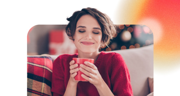 A woman in a red shirt sipping a warm drink. She is smiling contentedly.