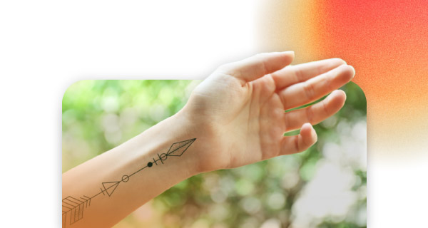 Someone holding their wrist outward, with an arrow tattoo pointing up their arm.
