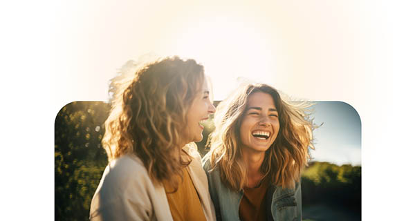 Two women laughing in the sunlight, enjoying each other's company.