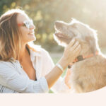 A woman petting her dog in the sunlight.