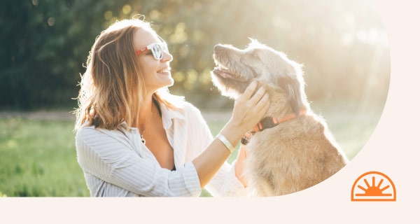 A woman petting her dog in the sunlight.