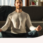 A man meditating in his living room in front of the couch.