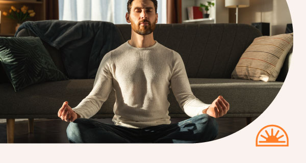 A man meditating in his living room in front of the couch.