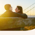 A loving couple sits on a bench as the sun sets,.