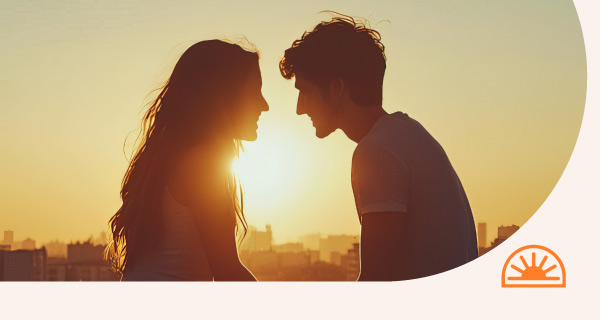 Two people standing in front of a sunset, looking deeply in love