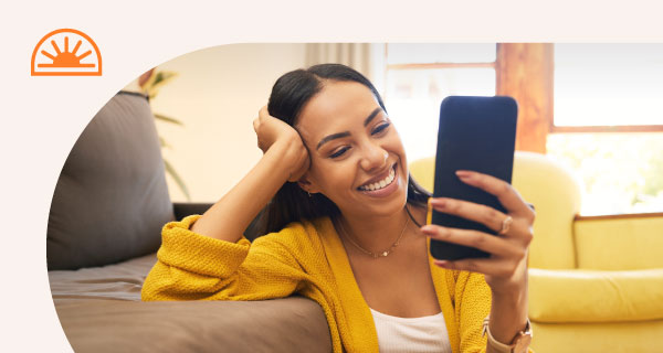 A woman smiling excitedly at her phone.