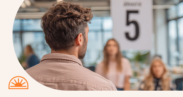 A man in an office building, a poster with the number 5 is in front of him.