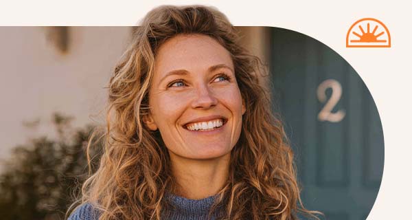 A woman standing outside her home. The house number is 2.