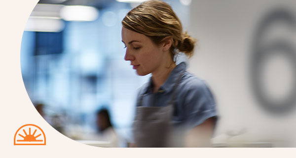 A woman in scrubs working in a hospital, with the number 6 on the wall behind her.